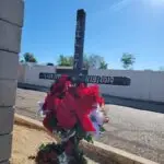 Roadside memorial for Bill J. Mussell, featuring a wooden cross decorated with flowers and personal tributes in a desert setting.