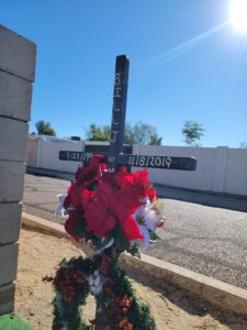 Roadside memorial for Bill J. Mussell, featuring a wooden cross decorated with flowers and personal tributes in a desert setting.