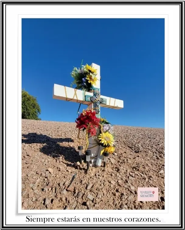 A white wooden roadside memorial cross for Francisco J. Fernán Martínez on the side of US-60 in Mesa, Arizona. The cross is adorned with colorful artificial flowers and a small framed photo of a man.