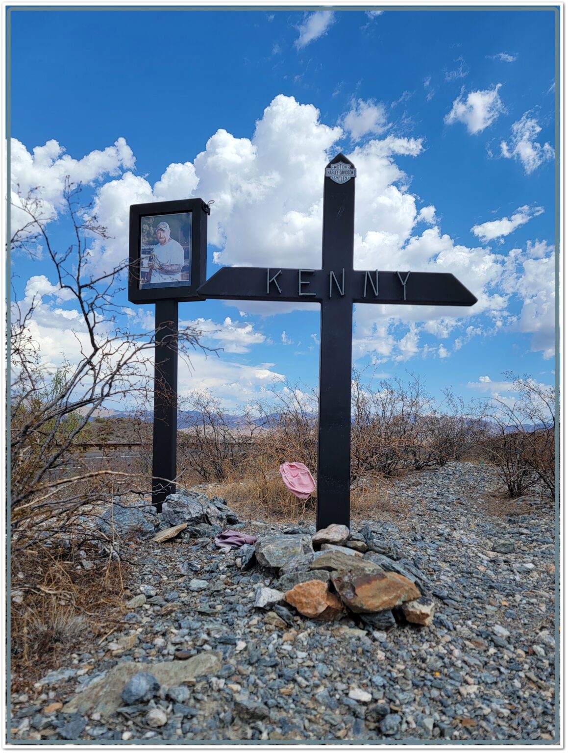Roadside memorial cross labeled “Kenny” with framed photo and Harley-Davidson emblem at Gonzales Pass mile marker 218