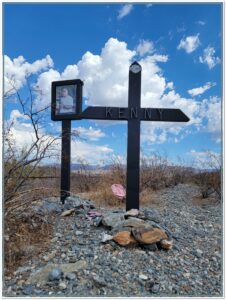 Roadside memorial cross labeled “Kenny” with framed photo and Harley-Davidson emblem at Gonzales Pass mile marker 218