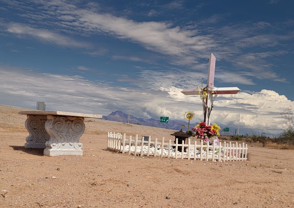 Roadside memorial with a white cross and fence near Freeway Exit 194.