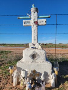 Roadside memorial for Russell, featuring a large white cross with a wooden base in a desert landscape
