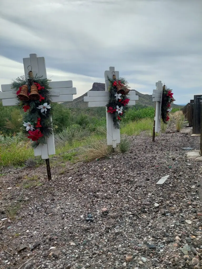 Three wooden roadside memorial crosses adorned with Christmas garlands and festive decorations in the Arizona desert landscape.