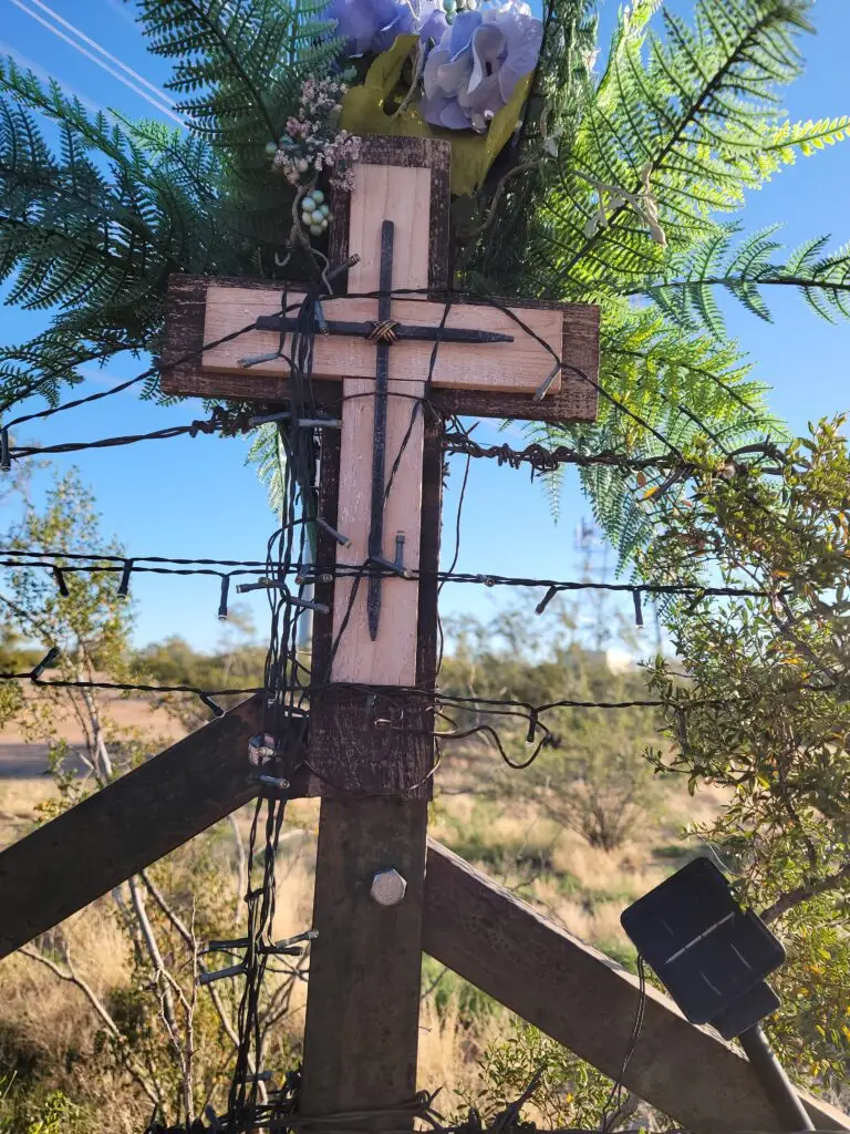 A white roadside memorial cross positioned against a black wire fence line in North Scottsdale, Arizona.