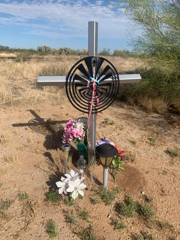 A roadside memorial featuring a large dreamcatcher and a cross on Highway 79 in Florence, Arizona, honoring a member of the Salt River Pima Indian Tribe.
